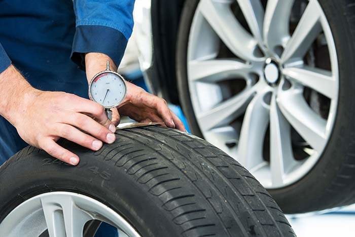 Mechanic, pressing a gauge into a tire tread to measure its depth for vehicle and road safety